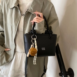 Detail of black pebbled leather bucket bag featuring knot handle and baseball charm pendant