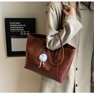 Brown leather tote bag featuring subtle litchi texture and a cute plush charm accessory