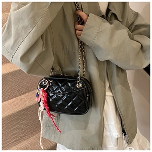 Detail of black quilted crossbody bag with golden chain and colorful braided pendant decor
