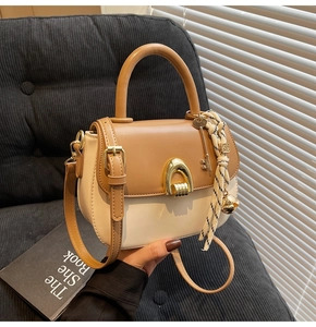Close-up of dual-tone leather handbag with horseshoe buckle and decorative keychain