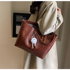 Detailed shoulder view of a large brown vintage leather tote bag with a fuzzy monster charm