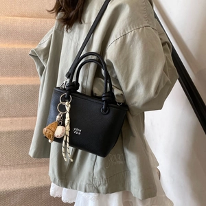 Detail of black leather bucket bag with rope handle and baseball charm on a model