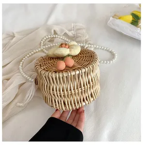 Detail of round straw bag featuring flower charms, cherry charms and pearl chain strap