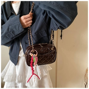Detailed view of dark brown quilted crossbody bag with gold chain strap and colorful charm