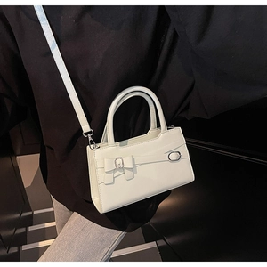Detail of cream crossbody bag featuring a decorative bow and silver metal buckle