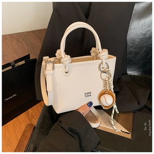 Close-up of white lychee textured tote bag with baseball charm and leather handle