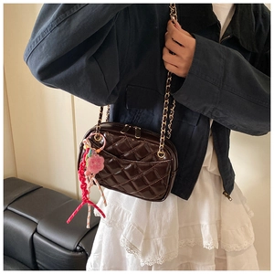 Detail of dark brown quilted leather crossbody bag with gold chain and woven charm