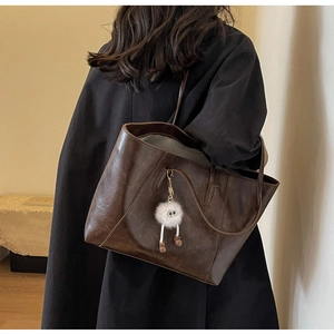 Detail of vintage brown leather tote bag with white plush monster charm on model shoulder