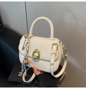Close-up of off-white leather handbag featuring a gold arc lock and decorative charms