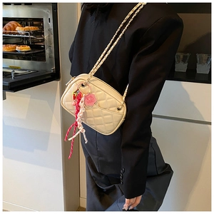 Close-up of off-white quilted crossbody bag with gold chain and floral charm detail