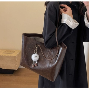 Detail view of large brown faux leather tote bag with a white plush monster charm