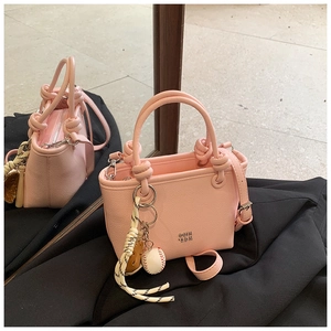 Detailed view of pink textured leather crossbody bag with metal logo and baseball charm