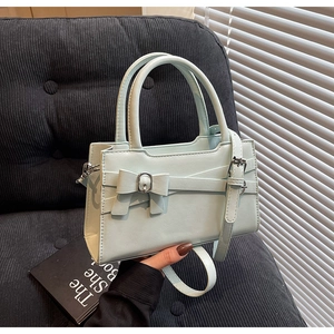 Detail of light green crossbody bag with bow buckle and cylindrical handles in hand