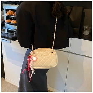 Detail of cream quilted crossbody bag with heart charm and woven strap on model back