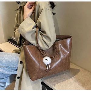 Detail of a large brown tote bag showing the distressed leather texture and plush charm