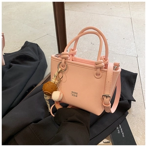 Macro view of pink pebbled leather bucket bag with knot handles and baseball keychain charm