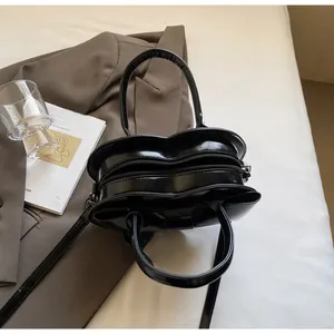 Glossy black heart-shaped handbag with bow detail on a stylish set with suit and books