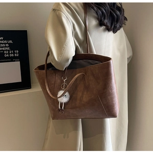 Brown leather tote bag featuring a cute plush charm and minimalist shoulder straps