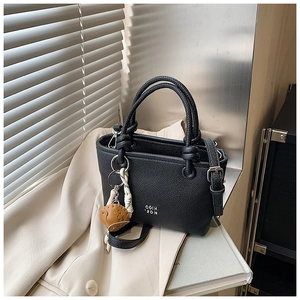 Detail of black litchi grain leather bucket bag with woven handle and brown glove charm