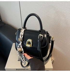 Detail of black saddle bag with golden horseshoe lock and decorative woven pendant