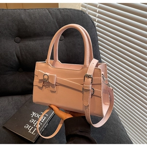 Pink crossbody bag with bow detail and silver buckle shown on a modern sofa background