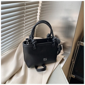 Detail of black lychee grain handbag with knotted handles and metallic logo on beige fabric