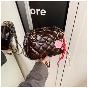 Detail of dark brown quilted crossbody bag with gold chain and woven lucky charm