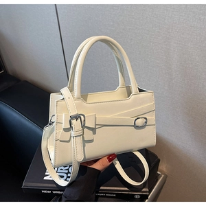 Detail of cream white leather handbag with bow decoration and silver buckle on a book