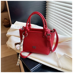 Detail of red lychee leather bag with knot handle and baseball charm on beige blazer