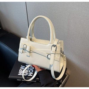 Detail of cream white leather handbag featuring belt buckle decor and adjustable strap