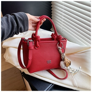 Detail of red lychee leather bucket bag with knotted handle and baseball charm decor