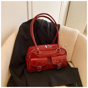 Detail of red patent leather pillow bag with silver buckles on beige sofa