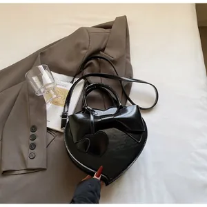 Detail of a black heart-shaped handbag with a large bow and glossy finish on a bed
