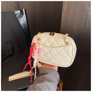 Detail of cream quilted leather crossbody bag with gold zippers and woven floral charm