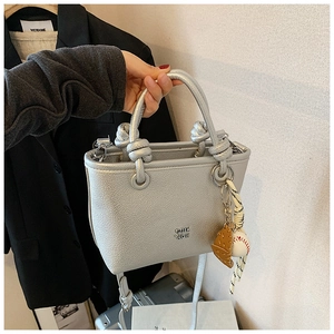 Close-up of a silver lychee grain tote bag featuring knot handle and baseball charm