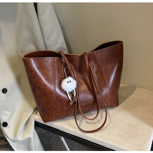 Close-up of brown leather tote bag with fluffy monster charm on a woven chair