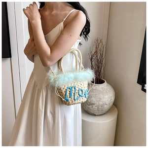 Detail of woven straw bucket bag with blue feather trim and pearl shoulder strap
