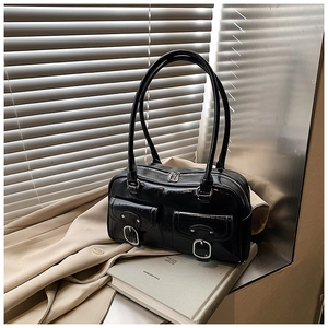Close-up of black glossy shoulder bag with silver buckle pockets on a beige trench coat