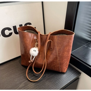 Detail of vintage brown tote bag with smooth texture and cute plush charm on a wooden desk