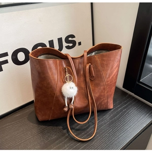 Detail view of large brown tote bag with leather texture and plush monster charm decoration