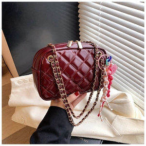 Close-up of wine red quilted handbag featuring golden chain strap and unique tassel charm