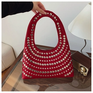 Détail du sac hobo en cuir rouge avec rivets argentés posé sur une table en bois