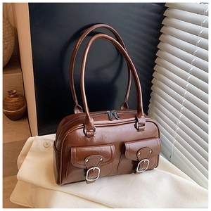 Close-up of brown glossy leather shoulder bag with dual front pockets and silver buckles