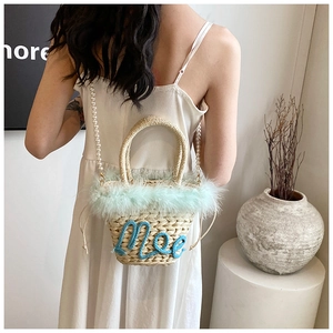 Detail of woven straw bucket bag with green faux fur trim and elegant pearl strap