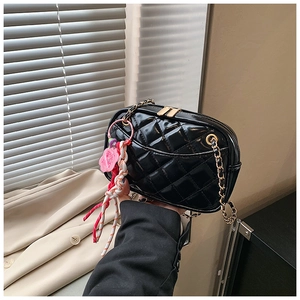 Detail of black quilted shoulder bag with golden chain and colorful charms in warm setting