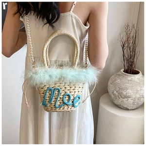Detail of woven straw bag featuring light green feather trim and blue Mee lettering