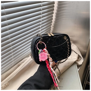 Detail of black quilted shoulder bag with shiny finish, gold chain strap and floral pendant