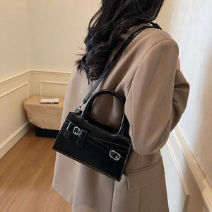 Chic black patent leather crossbody bag with bow detail worn by a model in a blazer