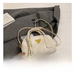 Détail du sac Boston crème avec logo en triangle métallique et foulard sur la poignée