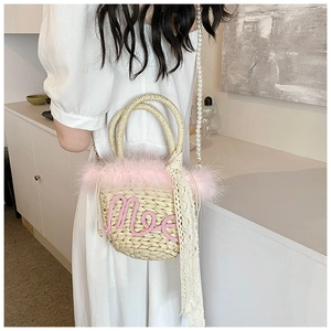Detail of woven straw bucket bag featuring pink feather trim and pearl bead strap